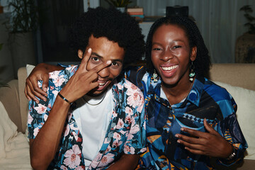 Cheerful Black couple in floral shirts taking selfie at home