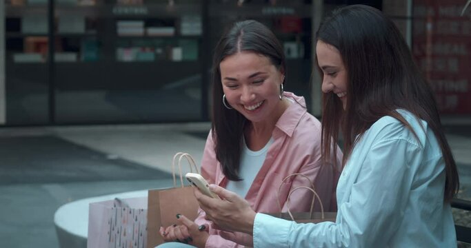 Two women friends sit bench close-up chatting using phones showcasing sincere friendship. Sincere friendship evident laughter shared stories Sincere friendship mix joy elegance connection.