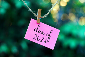 class of 2024 on pink note paper hanging on rope with bokeh background