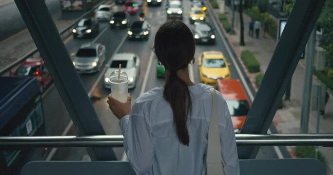 Woman in modern glass overhead crossing looking at traffic urban life unfolding below back view close-up. Overhead crossing haven above city streets Overhead crossing fusion of safety and future.