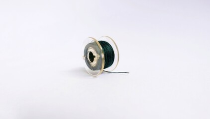 Close up photo of a sewing machine spool or bobbin made of clear plastic. Green thread coiled isolated on a white background.