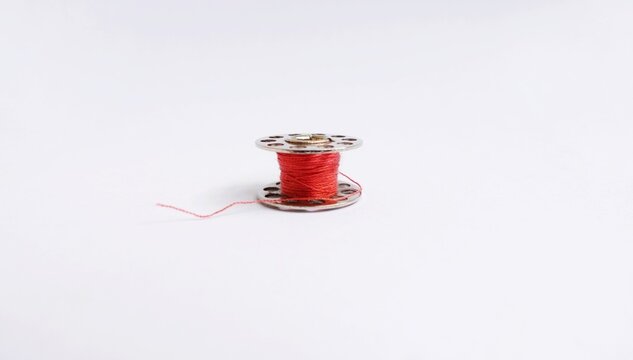 Close up photo of a sewing machine spool or bobbin made of metal. Red thread coiled isolated on a white background.