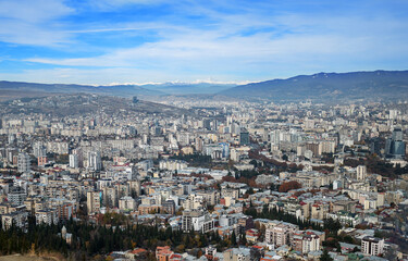 Fototapeta premium sprawling urban landscape of Tbilisi, Georgia, under a clear blue sky view showcases diverse architectural styles densely packed residential areas stretching towards the distant mountains