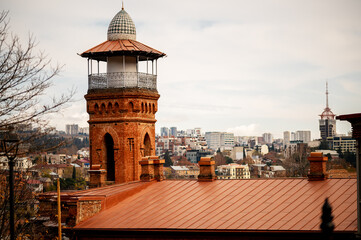 historic brick watchtower with a dome roof, set against the backdrop of modern Tbilisi’s urban skyline contrast between old and new architectural styles highlights the city's - obrazy, fototapety, plakaty