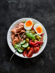 Delicious balanced lunch - grilled salmon, boiled egg, fresh vegetable salad on a dark background, top view