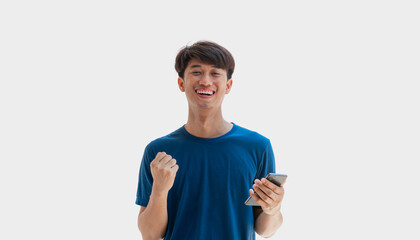 A handsome young Asian man smiling happily in a blue t-shirt is using his smartphone to shop online or chat with friends online. Man rejoicing from smartphone message winning lottery game.