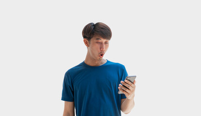 A young Asian man in his 20s wearing a blue t-shirt is excited with surprised by notification on his cell phone, isolated on gray background. Man is surprised by message he received on his smartphone