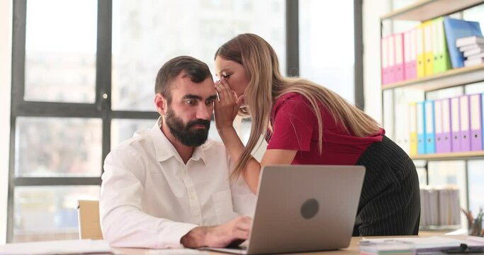 Businesswoman murmurs important information into ear of man