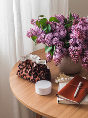 Aesthetic women's table - cosmetic bag, cream, notebooks and a bouquet of lilacs on a wooden table