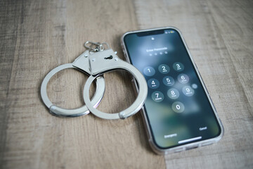Phone showing security password on screen and handcuffs on wooden background. Cyber crime concept.