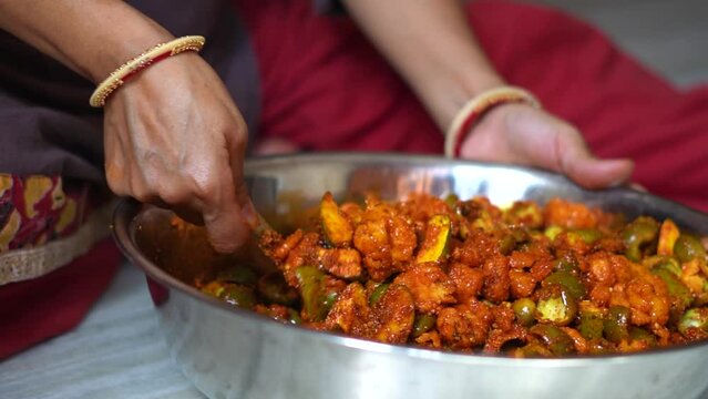 Hands of Indian woman wearing bangles mixing raw mangoes with spices to make Mango pickles. Homemade organic pickle. Female preparing food in kitchen. An Indian housewife making pickle, household work
