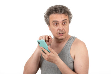 A gray-haired, shaggy, unshaven middle-aged man in a sleeveless T-shirt holds a smartphone
