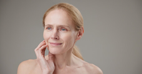 Real people - age, beauty, health and dry skin care concept - beautiful mature Caucasian middle aged woman in her 50s touching her face skin with a slight smile and good mood