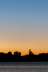 Silhouette land and trees on horizon under colourful sunrise sky