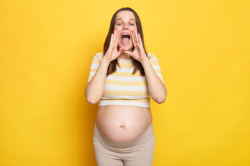 Screaming excited young Caucasian pregnant woman dressed in top posing against bright yellow wall...