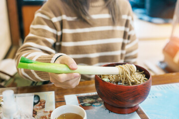 Woman tourist eating Negi Soba or Buckwheat noodles with a raw leek instead of chopsticks, famous...