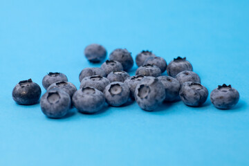 Organic blueberries in glass bowl on blue background, front view. Concept of vegan, freshness, natural food