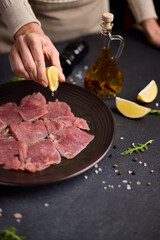 tuna carpaccio - woman squeezes fresh lemon juice onto slices of fresh raw tuna fillet on black ceramic plate