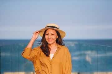 Naklejka premium Portrait image of a young woman with hat, hair blows in the wind, glass terrace with sea and blue sky background