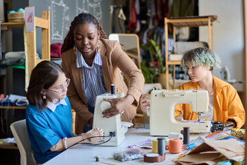 Portrait of Black young woman teaching girl with disability using sewing machines in vocational...