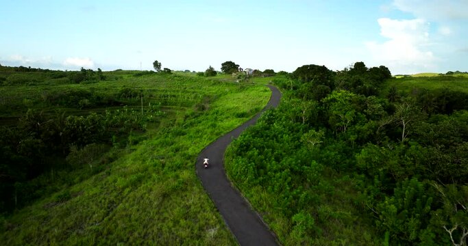 Girl in white drives scooter uphill while exploring Teletubbies Hills, Bali