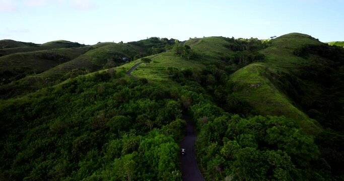Scooter drives through lush forested area up Teletubbies Hills, Bali. Drone