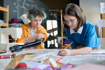 Portrait of two teenage girls with disability sewing clothing together in vocational training class