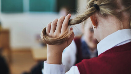 A girl touches a ponytail of her hair during class.