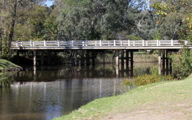 Bridge with white railings extending over water surrounded by trees and grass at Seven Creeks Park in Euroa, Victoria, Australia