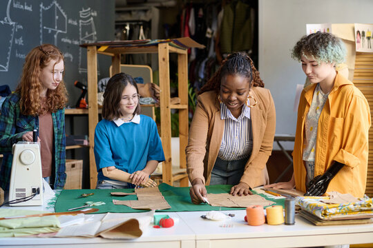 Portrait of Black young woman teaching diverse group of girls making clothing patterns in sewing class