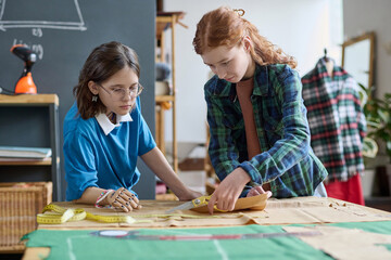 Portrait of two teen girls making clothing patterns together in sewing class at atelier copy space