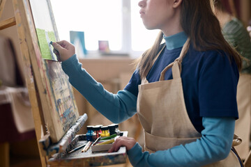 Cropped side view of young girl with disability drawing picture on easel and enjoying art therapy...