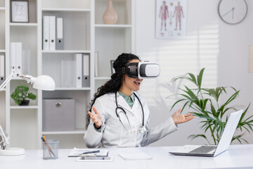 Excited Hispanic female doctor using virtual reality headset at her desk in a well-equipped medical...