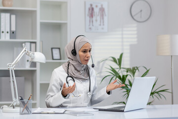 A professional Muslim female doctor is communicating with a patient through a video call, using a...