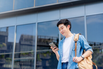 Portrait of handsome Asian student using smartphone. A young man standing outdoor happy smiling...