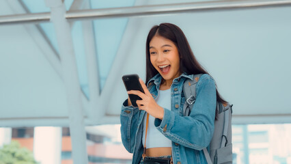 Young asian woman using mobile in city. Happy female tourist wearing jeans jacket and holding...