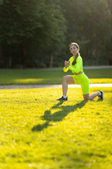 A woman in a neon yellow outfit is doing a yoga pose on a grassy field