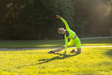 A woman in a neon green outfit is doing a yoga pose on a grassy field