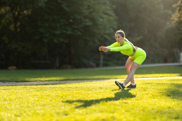 A woman in a neon yellow outfit is stretching on a grassy field