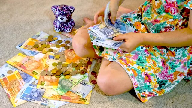 Girl counts South African one hundred rand banknotes next to spread out money
