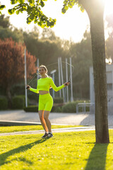 A woman in a neon yellow outfit is jumping rope in a park