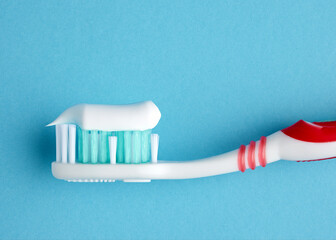Macro close up view of a plastic toothbrush with toothpaste on blue background.