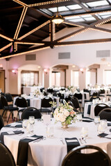 A modern reception venue with black napkins and white tabletops and wood beams.  