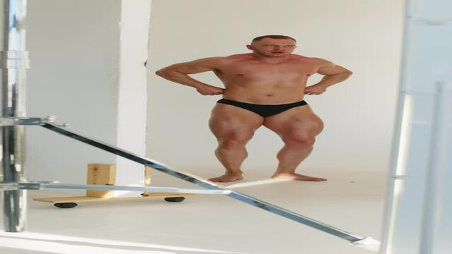 Vertical full shot of Caucasian male bodybuilder in underwear posing for camera showing muscles while shooting for magazine cover in photo studio