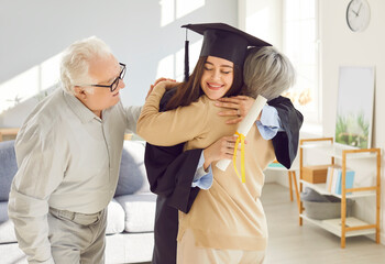 Portrait of a happy smiling graduate girl student hugging with her senior old parents holding...