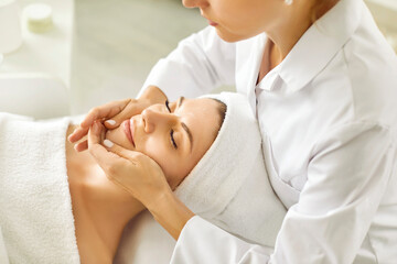 Portrait of pretty relaxed young woman lying with closed eyes having facial massage in spa salon....