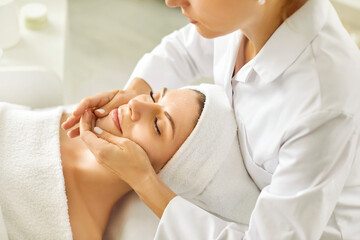 Naklejka premium Portrait of pretty relaxed young woman lying with closed eyes having facial massage in spa salon. Female client enjoy receiving skin care procedure treatment. Wellness and beauty day concept.