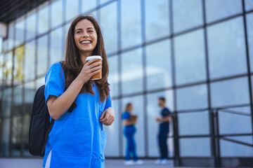 While walking to work in a city hospital, a young female nurse holding coffee to go.  Female...