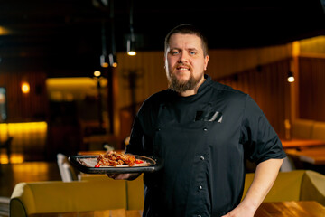 in a restaurant a chef in a black jacket stands smiling with a prepared Chicken wings
