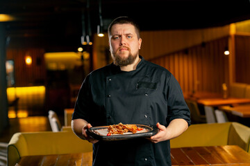 in a restaurant a chef in a black jacket stands with a prepared Chicken wings